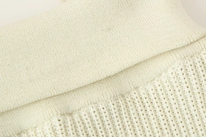 Detailed close-up of cream knit top featuring ribbed edges and openwork crochet texture