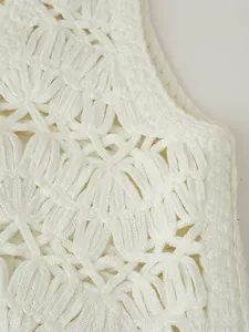Detailed close-up of white crochet vest featuring intricate hollow floral patterns and shells