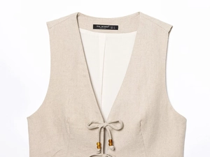 Detail of beige linen vest featuring V-neckline, tie closure and wooden bead accents
