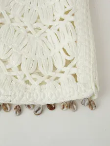 Detailed close-up of white crochet vest featuring natural shell fringe and bohemian textures