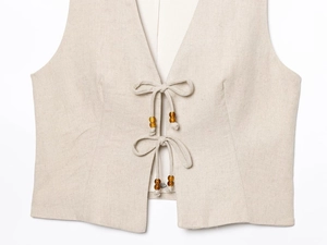 Detail of linen vest featuring bead-trimmed ties and natural woven fabric texture