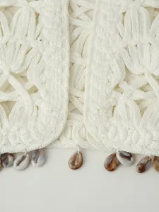 Detail of white crochet vest featuring shell charms and bohemian hollow-out patterns