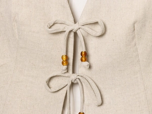Detail of beige linen vest with beaded tie closure and natural fiber texture