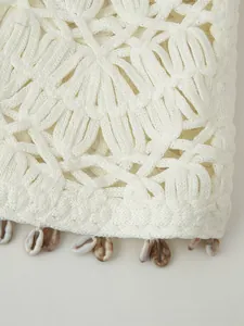 Detailed close-up of white crochet vest featuring shell charms and hollow knit patterns