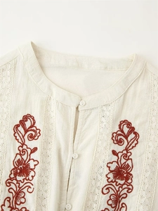 Détail de la broderie florale rouge et de la dentelle sur chemisier en lin écru