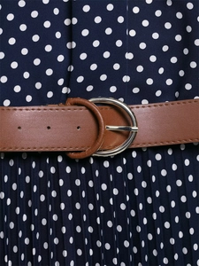 Dettaglio di un abito a pieghe a pois con cintura in pelle marrone e fibbia d'argento