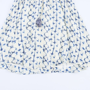 Detail of V-neck dress featuring blue tie-dye pattern and a two-tone tassel pendant