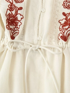 Détail du chemisier en coton beige avec broderies florales rouges et finitions en dentelle