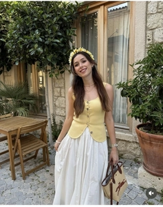 Detail of yellow knit vest with vintage buttons and white pleated skirt for summer fashion