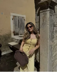 Close-up of yellow knit tank top with buttons and woven handbag in a street setting