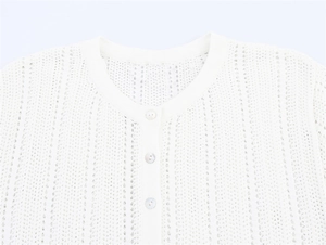 Detail of white crochet knit top showing round neck and pearlized buttons texture
