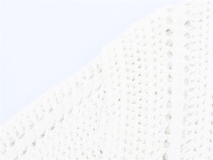 Detail shot of white crochet knit fabric with intricate hollow patterns and textures