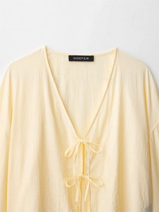 Detail of cream V-neck blouse with textured crinkle fabric and delicate front tie-up bows