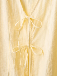 Detail of pale yellow crinkle fabric with V-neckline and delicate tie-up bow closure