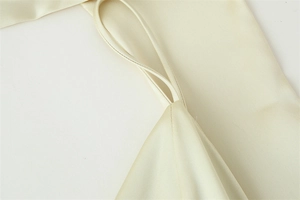 Macro shot of cream satin dress featuring thin straps and delicate pleated sewing details