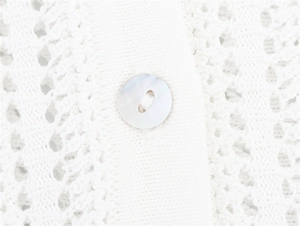 Close-up of white crochet texture featuring a pearlescent button with iridescent finish