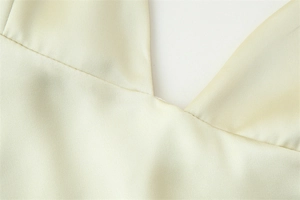 Close-up of a smooth light yellow satin dress showing fine V-neck stitching and silk texture