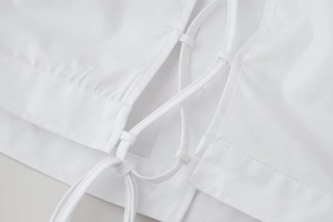 Macro view of white cropped shirt showing criss-cross lace-up back detailing and stitching