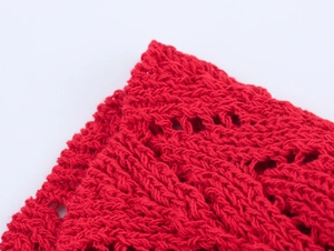 Macro detail of red knitted V-neck dress featuring delicate ruffle hem and crochet texture