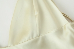 Macro detail of cream satin dress fabric showing fine stitching and thin shoulder straps