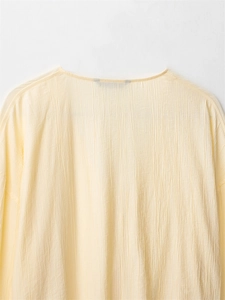 Detail of light yellow textured crinkle fabric on long sleeve blouse with crew neck