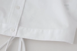 Detailed close-up of white cropped shirt showing buttons, stitching, and hem tie details