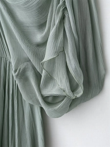 Detailed close-up of sage green pleated chiffon fabric with ruffled sleeve cuffs