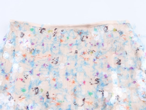Close-up of the light blue and white sequins on a beige mesh skirt with satin edge details