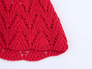 Detailed close-up of red knit dress showing intricate hollow wave pattern and V-neckline texture