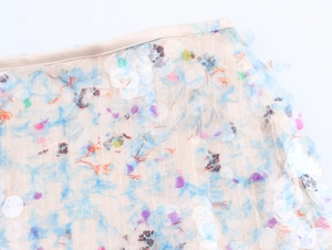 Detail of sheer beige mesh skirt with colorful sequins and subtle floral print texture