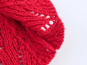 Macro detail of red knit dress showing hollow crochet pattern and soft wool texture