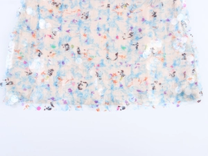 Detail shot of sheer beige fabric with blue floral print and iridescent round sequins