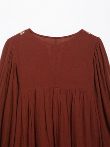 Detail view of brick red cotton linen fabric with colorful shoulder embroidery and pleats