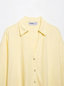 Detail of classic lapel V-neckline and wood-textured buttons on pale yellow linen shirt