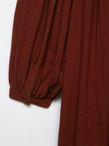 Close-up detail of rust red embroidered cotton dress with pleated cuffs and tiny button