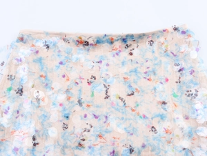 Close-up of beige mesh fabric with blue sequins and colorful floral patterns