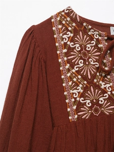 Close-up of intricate embroidery and drawstring neckline on rust red boho top
