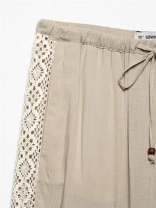 Detail of linen trousers featuring drawstring waist and delicate white lace stitching