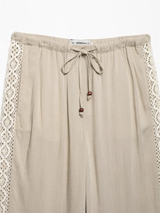 Detailed view of beige wide-leg pants with elastic drawstring waist and lace trim