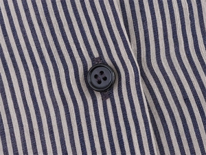 Macro detail of a black button on blue and white striped linen blend shirt fabric