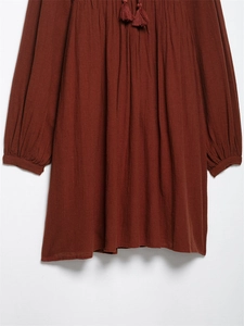 Detail of rust red embroidered cotton dress featuring tassel neck ties and elastic cuffs