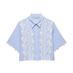 Detail of light blue shirt featuring floral embroidery and scalloped lace hem