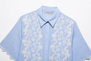 Close-up of intricate white floral embroidery and wavy hem on light blue cotton shirt