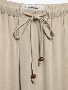 Detail of linen pants featuring an elastic drawstring waist with decorative wooden beads