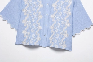 Detailed embroidery on light blue shirt featuring floral patterns and scalloped edges