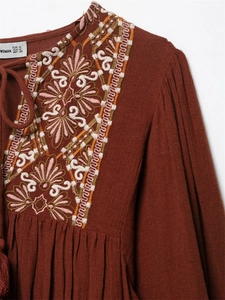 Detail shot of boho floral embroidery and tassel neck on a red-brown cotton dress