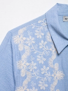 Close-up of white floral embroidery and cotton linen texture on a light blue lace shirt