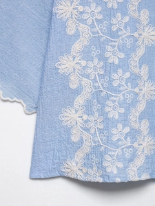 Detailed view of light blue shirt with white floral embroidery and scalloped edges
