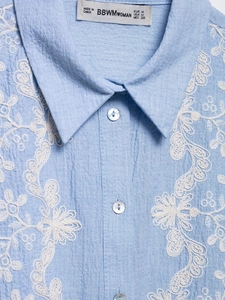 Detail of white floral embroidery on light blue linen shirt with pearlescent buttons