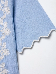 Detail of light blue fabric with white floral embroidery and scalloped cuff design